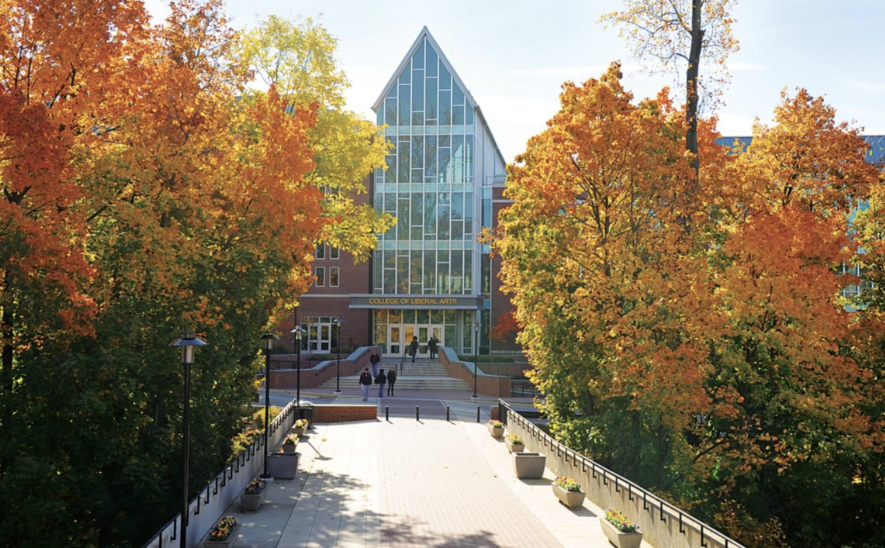 A building with a glass cathedral-style face and autumn trees on both sides of the photograph, orange and yellow.